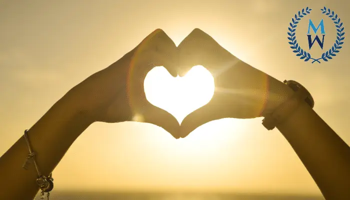 hands making heart shape with sun setting in the background