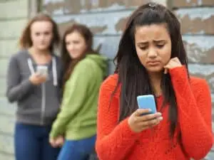 How to deal with cyberbullying: Signs, effects, and more children mocking girl on phone at school