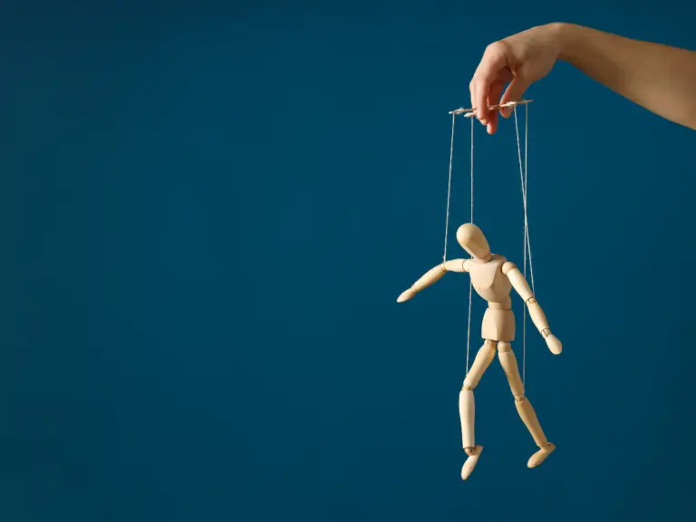 A wooden puppet being held up by a hand and strings, symbolizing controlling behavior.