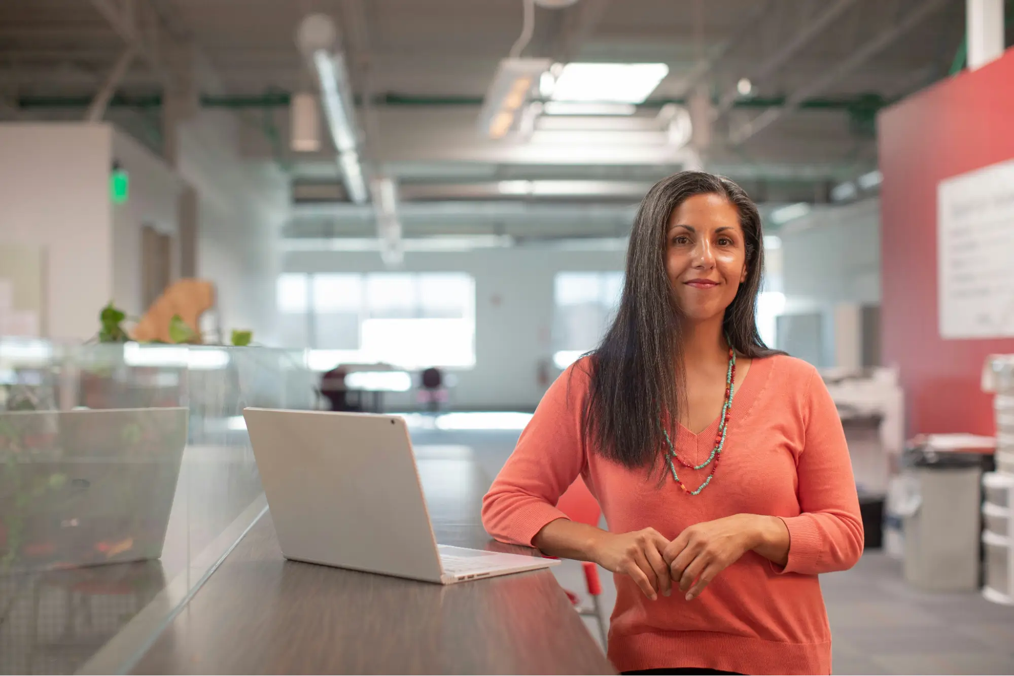 A confident woman standing at her workspace with a laptop, representing how to set boundaries at work by knowing your limits and communicating them clearly.