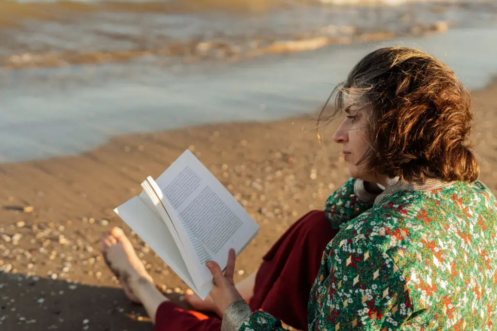 A woman sits on a beach reading a book to show how to increase dopamine by stimulating your brain.