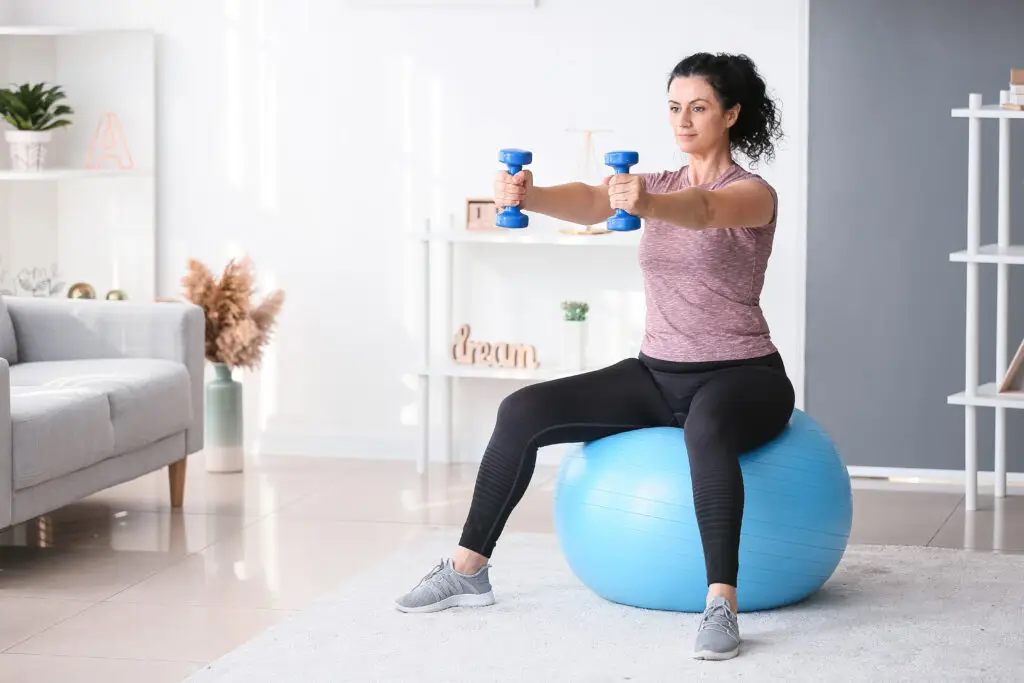 A woman sits on a blue exercise ball with weights in her hands, showing how to increase your dopamine with exercise.