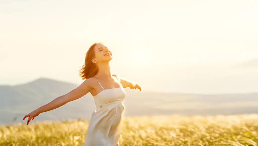 A woman is walking in a field on a sunny day with her arms out to her sides showing her increased serotonin.