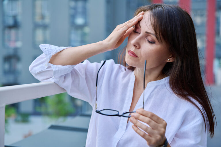A woman holding glasses in her hand with her other hand on her head showing that she is anxious.
