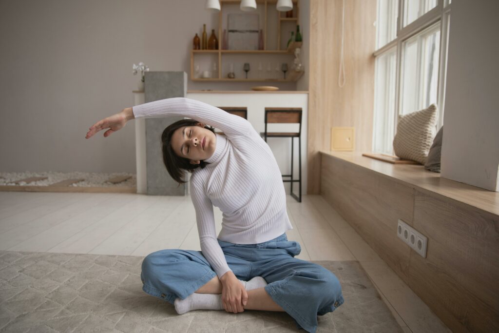 A woman is sitting and stretching her arm over her head to stimulate progressive muscle relaxation, one of the most effective vagus nerve exercises.