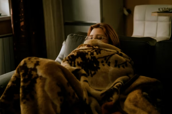 A young woman experiencing apathy, sitting under a blanket, peeping over with glasses