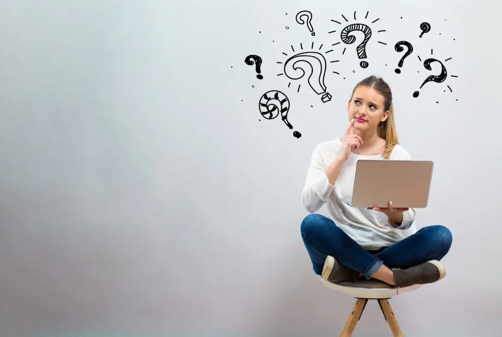 A woman sitting on a chair holding a computer with question marks above her head pondering what is causing her lack of executive functioning skills.
