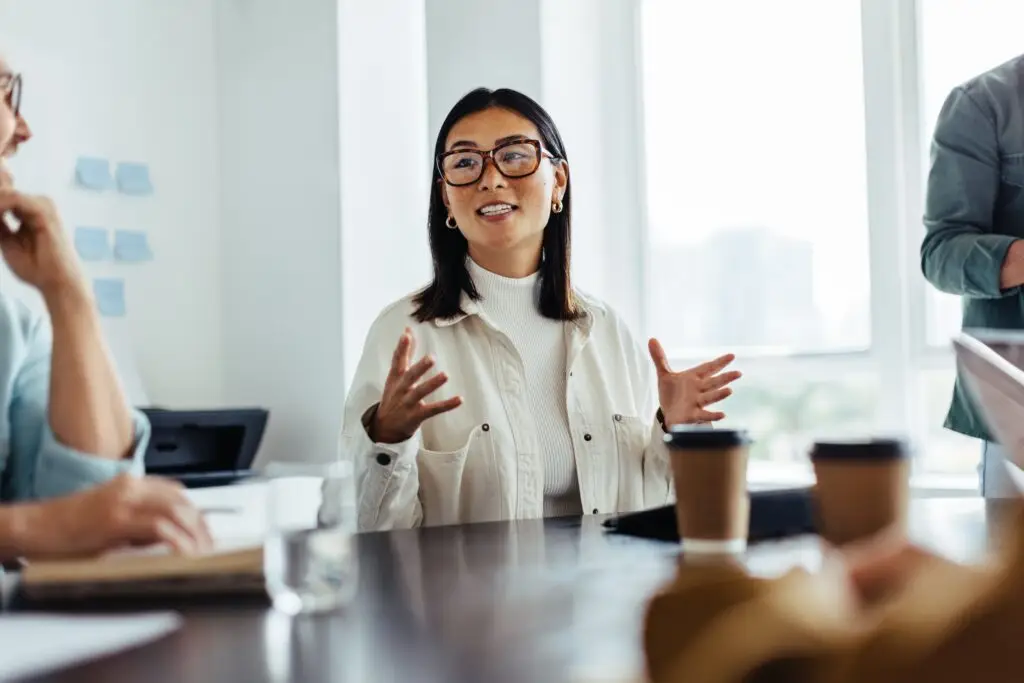 A middle-aged asian woman confidently addressing workplace toxicity during a work meeting.