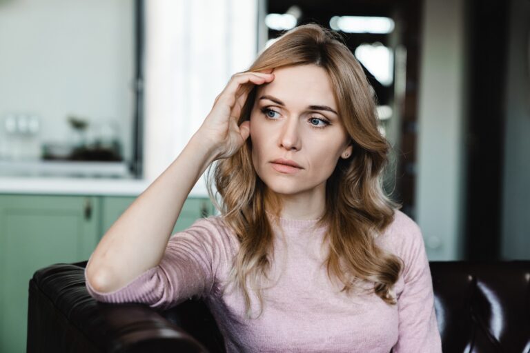 A young blonde-haired woman holding her hand to the side of there head while she thinks about needing to take an online eating disorder test.