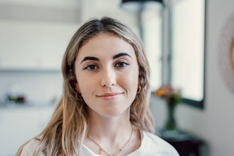 A young blonde woman looking at the camera in peace, smiling because she learned how to control her emotions.