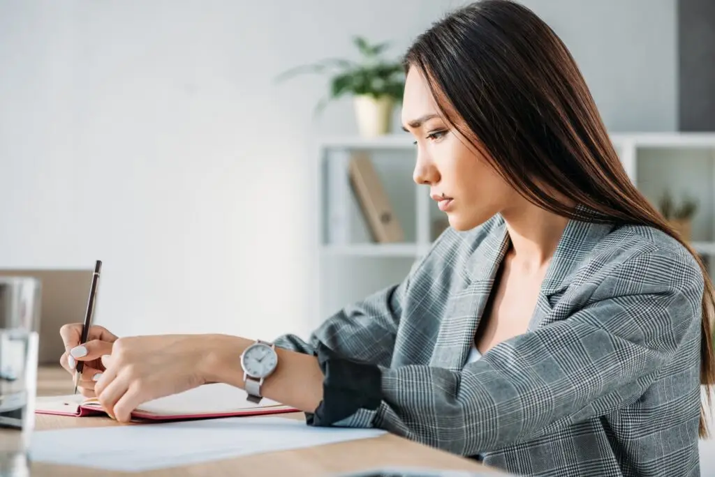 How to stop overreacting and finally gain control over your emotions A young trendy asian woman writing on paper, trying to understand her emotional triggers.