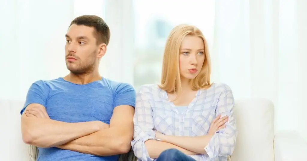 A young couple sitting next to each other, folded arms, avoiding necessary conflict