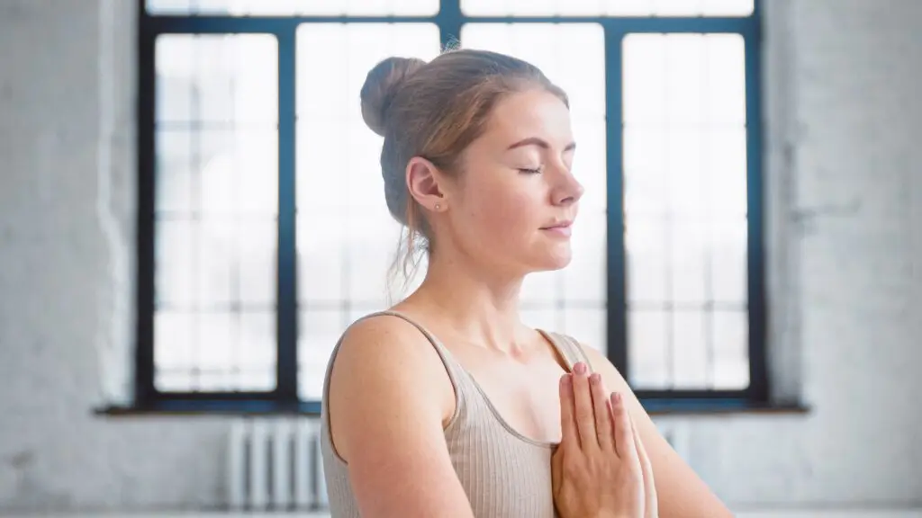 What to do when you're feeling unappreciated a young woman meditating, hands to heart, eyes closed, validating her feelings.