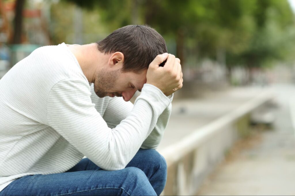 A young man with his hands on his head, grieving a significant loss.