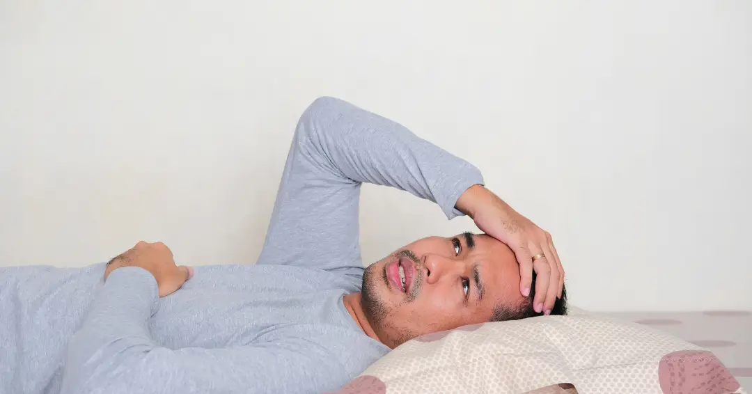 Man laying on his back with his right hand on his head, looking worried and wondering how to stop overthinking.