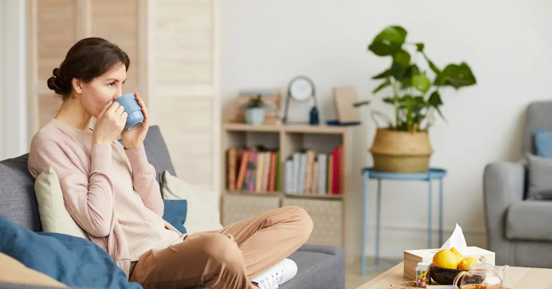 Woman sitting on a sofa in her living room, smiling and sipping a drink from a mug, grateful that she now has tips on how to stop overthinking.