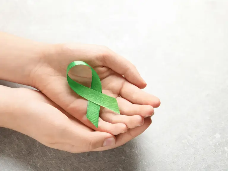 A hand holding a green ribbon symbolizing Mental Health Month