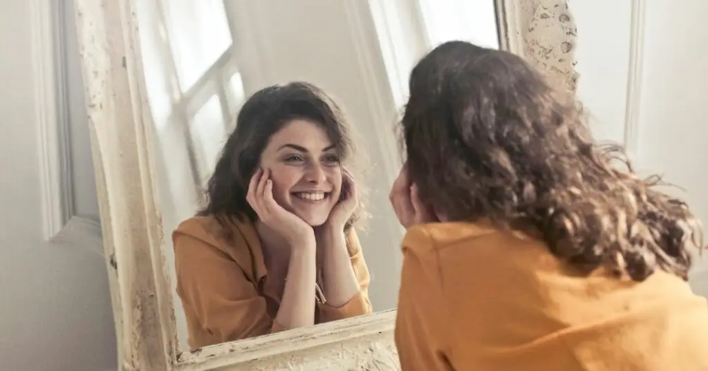 A young woman is looking at herself in the mirror and smiling. This shows that there are ways to manage depression.