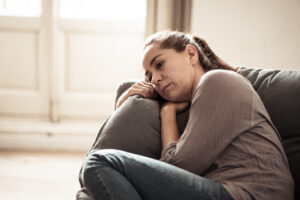 Woman sits on couch holding a pillow and looking sad representing one of the emotional symptoms of depression.