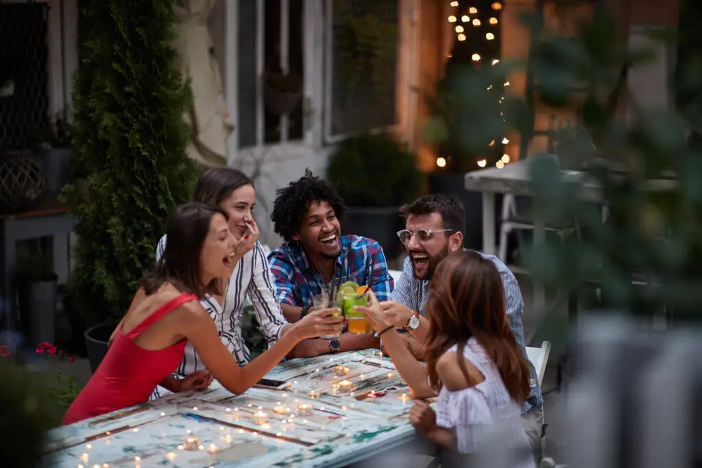 Introvert vs Extrovert: How to embrace your authentic self group of five adults making toast with cocktails, at the outdoor bar, laughing, having fun. Fun, party, socializing, extrovert persons
