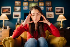 Woman on couch with her head in her hands and eyes closed struggling with high functioning anxiety.
