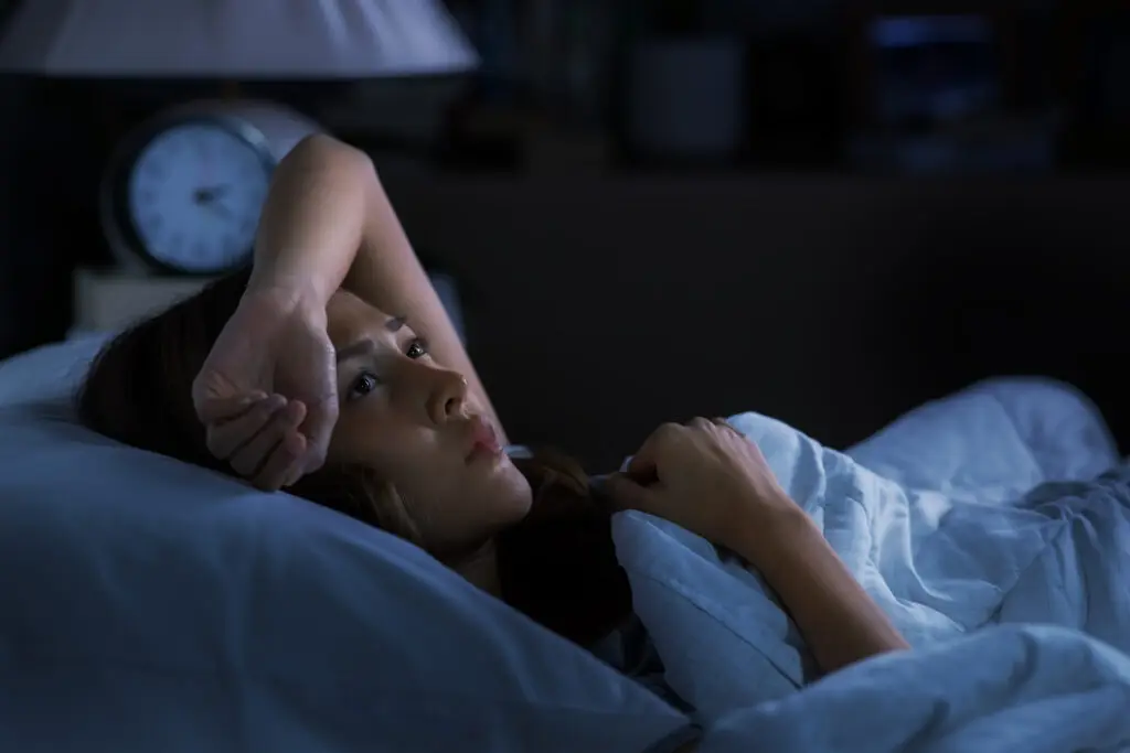 7 Signs of High Functioning Anxiety: Plus How To Relieve Some Of That Anxiety Woman lying in bed in the dark with insomnia as a physical symptom of high functioning anxiety