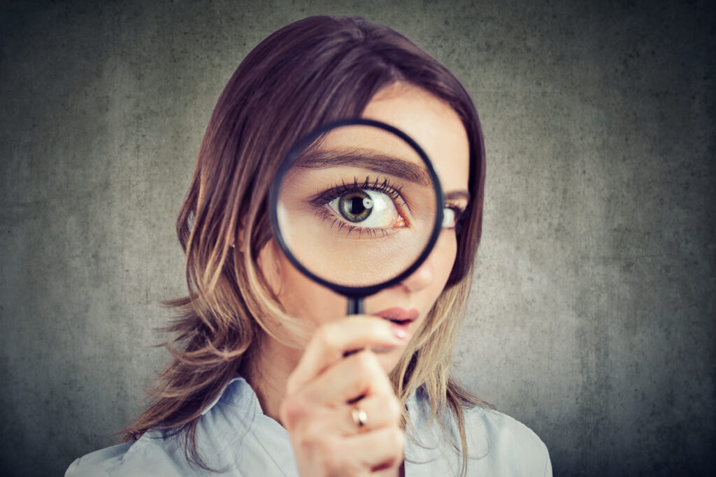 What is ADHD Paralysis? Discover 10 Ways to Rebound A young woman peering into a magnifying glass, as a visual representation of someone trying to dig deeper into ADHD paralysis.