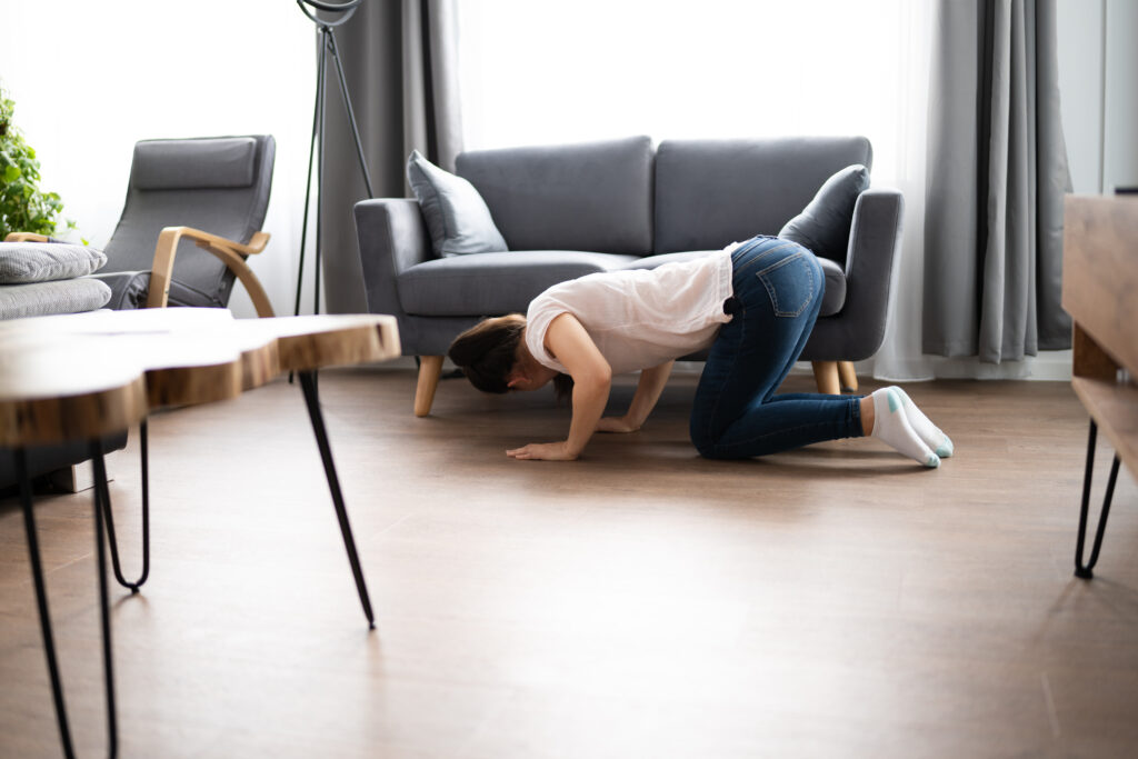ADHD Object Permanence: What it Really Means and 7 Essential Tips on Managing It It can be difficult to keep track of things when you have ADHD. This woman is peering under a couch with a confused expression.