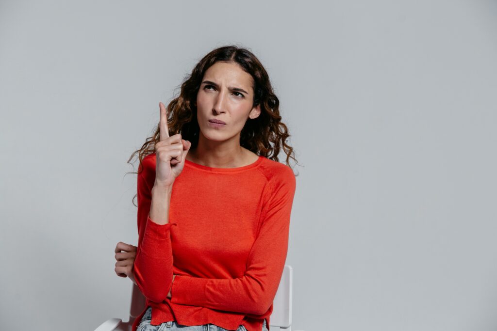 The Faux Pas of the Freudian Slip: What Causes It? A woman in a red sweater with a quizzical look and her hand in the air wondering how Freudian slips happen.
