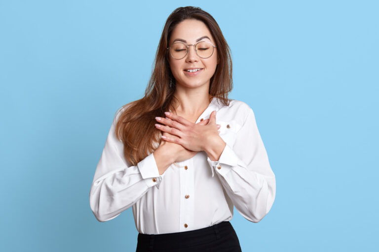 Makin Wellness Articles A woman holds her hands over her chest with a look of satisfaction on her face, representing the feeling a covert narcissist gets when they are encouraged by others.