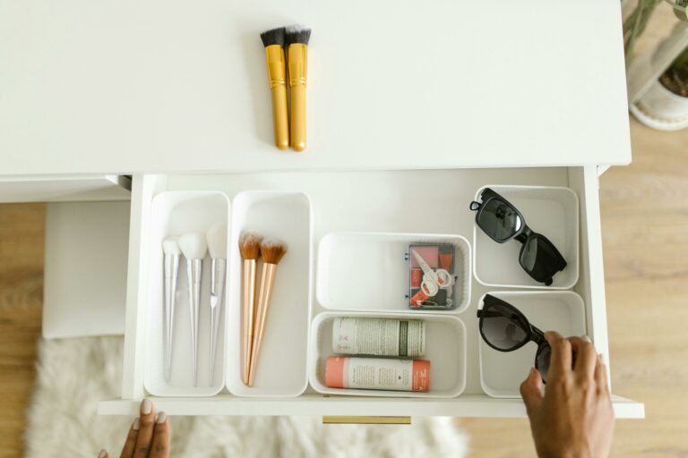 A neatly organized white drawer containing makeup brushes, sunglasses, and self care items, symbolizing how reducing clutter can help prevent feeling overstimulated.
