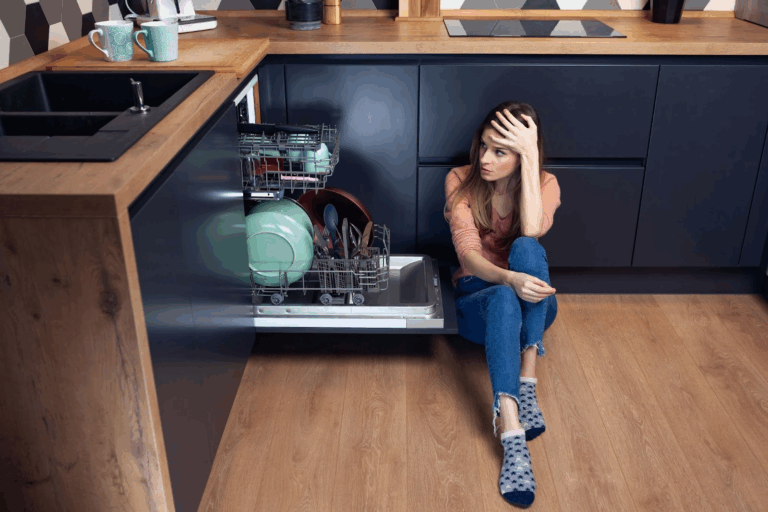 Woman sitting in front of a loaded dishwasher, illustrating the toll weaponized incompetence can take on those in a household.