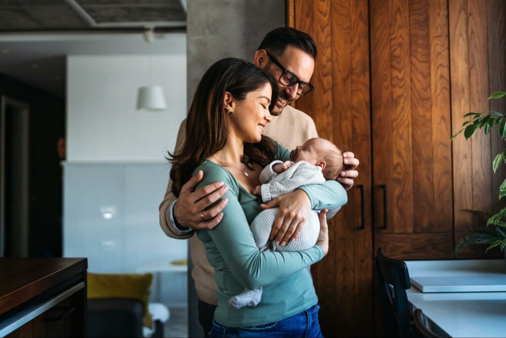 Happy young mother and father holding their newborn baby at home, representing the monogamy meaning and the stability it brings to family life.