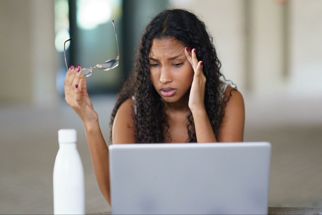 A woman experiencing mental overload while working at a laptop, illustrating how avoiding emotions long-term creates depression and higher stress.
