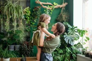 Mother helping her young daughter experience healthy identity formation, surrounded by plants.