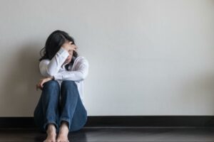 Distraught young woman sitting on the floor, holding her head and wondering, "What is a panic attack vs anxiety attack?"