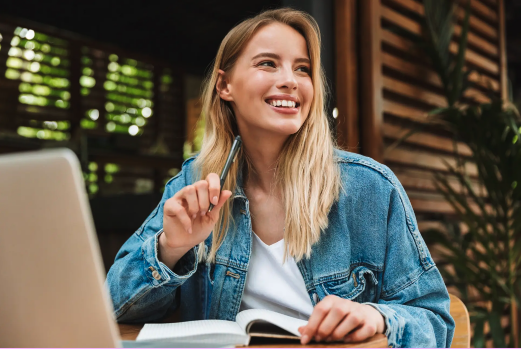 Young blond woman in a jean jacket, journaling and reflecting in a notebook, demonstrating how to practice mindfulness through writing.