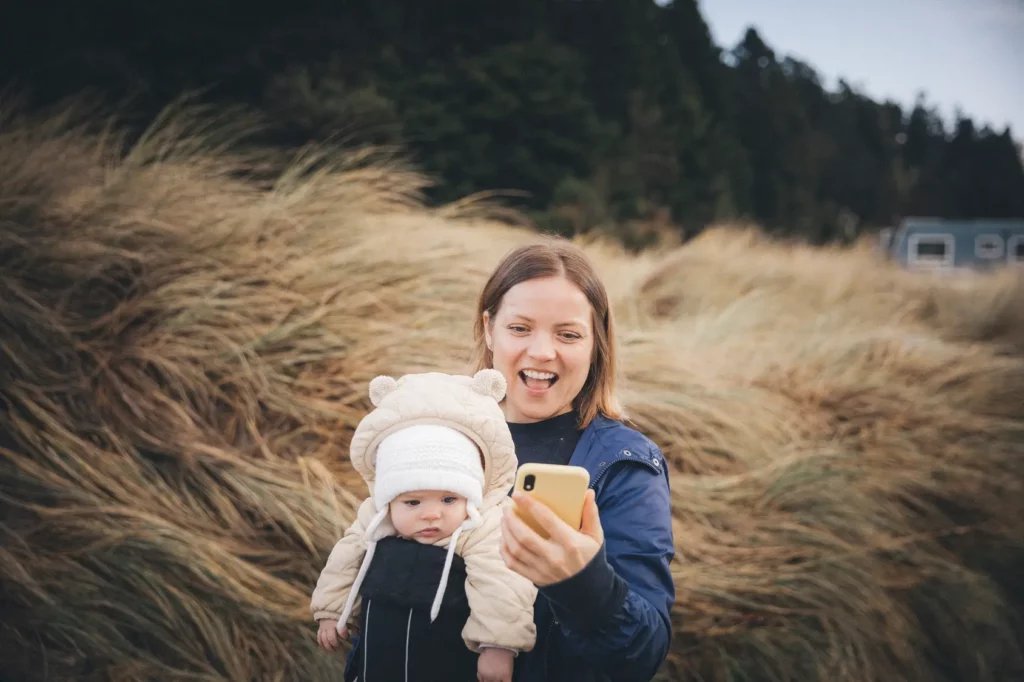 Woman enjoying using her phone while her baby looks on creating a question about where lack of self esteem comes from related to social media and technology.