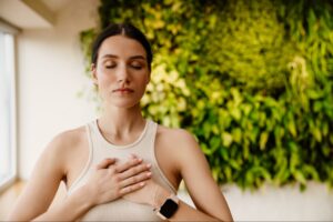 Young white woman demonstrating how to practice mindfulness, with her hands resting gently on her heart while controlling her breath.