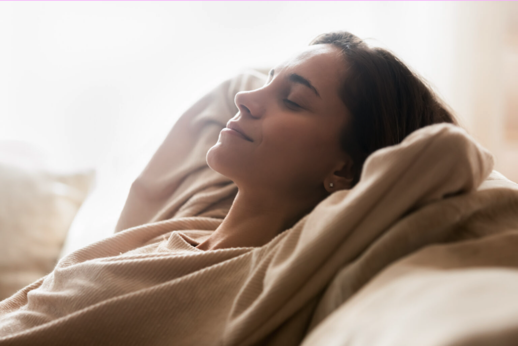 Young woman resting on a couch with eyes closed, appearing calm and relaxed.