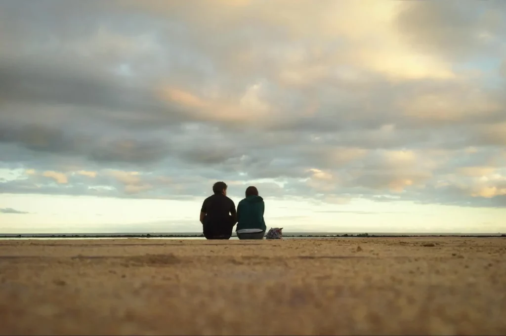Couple realizing that they would benefit from online therapy for relationship issues as they sit on a quiet beach and wonder when their relationship started to erode.