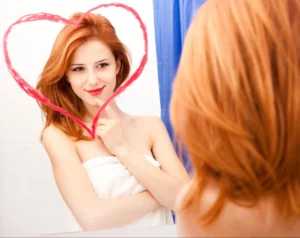 A woman smiling in the mirror after learning how to improve self esteem in different ways.