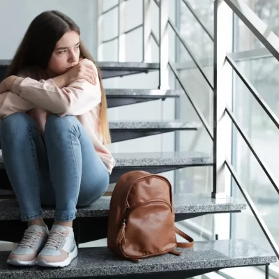 Young girl sitting on steps with her backpack, struggling with both ADHD and social anxiety.