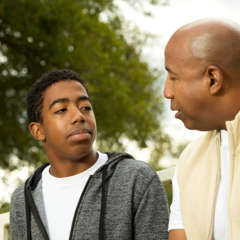 African American father and son in deep conversation about teen therapy. teen therapy