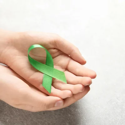 A hand holding a green ribbon symbolizing Mental Health Month