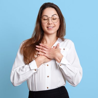 A woman holds her hands over her chest with a look of satisfaction on her face, representing the feeling a covert narcissist gets when they are encouraged by others.