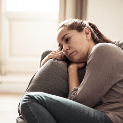 Woman sits on couch holding a pillow and looking sad representing one of the emotional symptoms of depression.