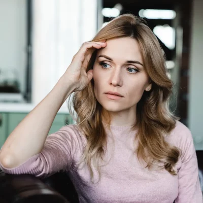 A young blonde-haired woman holding her hand to the side of there head while she thinks about needing to take an online eating disorder test.