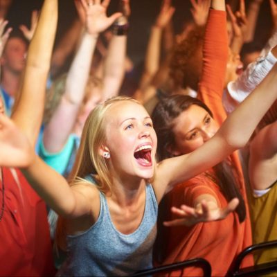 A tightly packed crowd at a live music concert with arms raised and people cheering, illustrating deindividuation as individuals blend into the collective energy of the group.