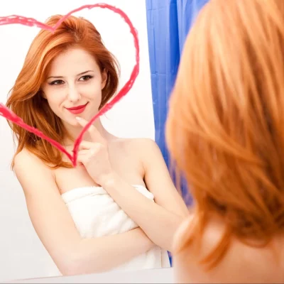 A woman smiling in the mirror after learning how to improve self esteem in different ways.